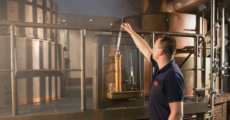 Brouwer controleert het brouwproces tussen de koperen ketels van de bierbrouwerij